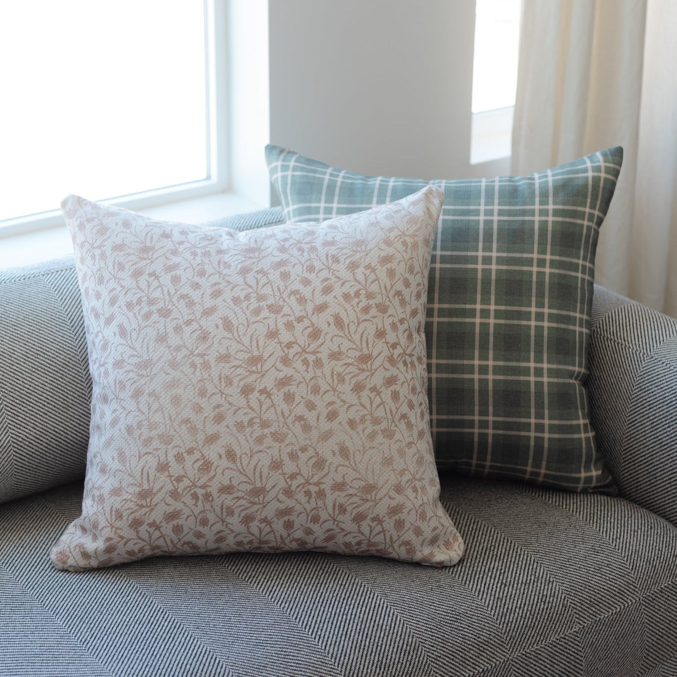 Beige floral patterned throw pillow displayed on gray textured sofa with plaid and striped pillows.