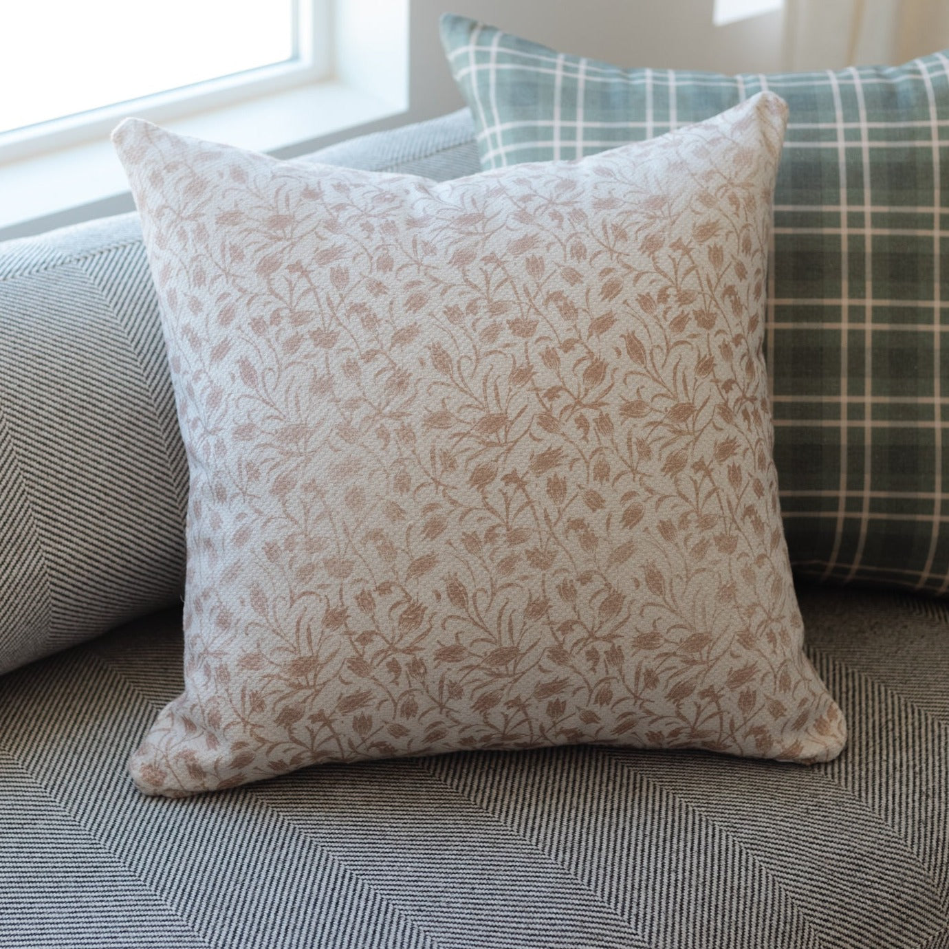 Square throw pillow with tan and cream floral pattern, displayed on textured furniture.