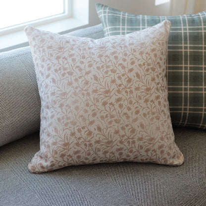 Square throw pillow with tan and cream floral pattern, displayed on textured furniture.