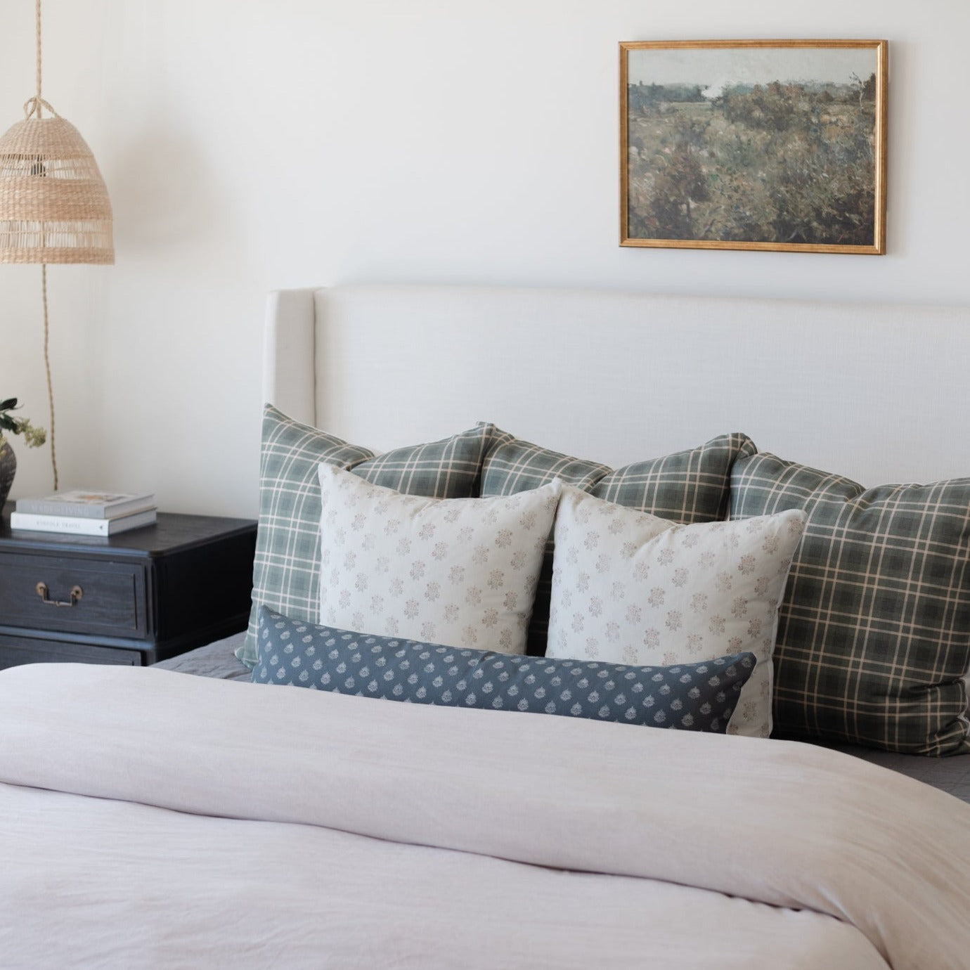 Blue lumbar pillow with small dot pattern displayed on a bed with plaid and floral pillows.
