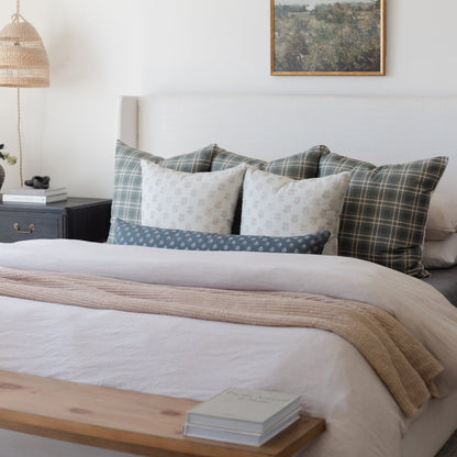 Bed styled with white linens, tan textured throw, and assorted plaid and patterned pillows in neutral tones.