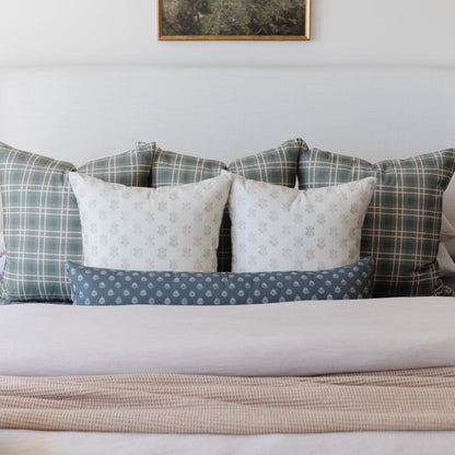 Bed styled with plaid and patterned throw pillows in gray and cream tones, layered with white and blue bedding.