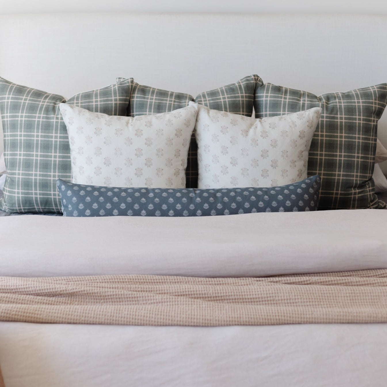 Decorative pillows arranged on a bed, featuring plaid, floral, and polka dot patterns in cream, gray, and blue tones.