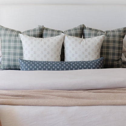 Decorative pillows arranged on a bed, featuring plaid, floral, and polka dot patterns in cream, gray, and blue tones.