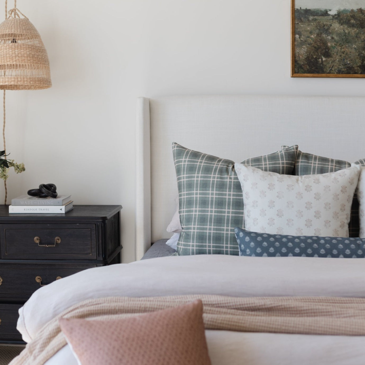 Bed with white upholstered headboard, layered pillows in plaid and floral patterns, and textured bedding in neutral tones.