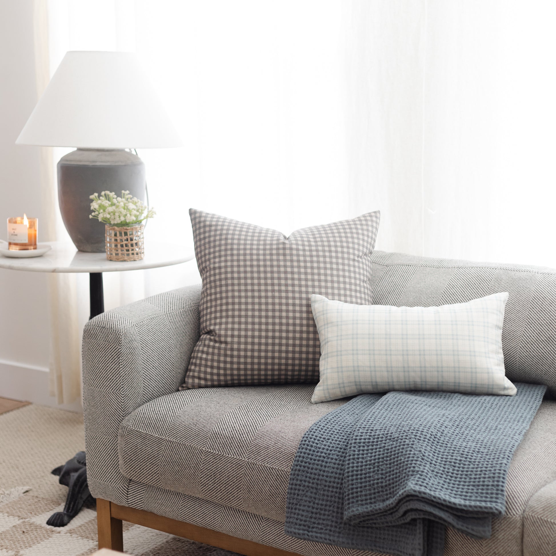 Gray and white gingham lumbar pillow displayed on a light gray upholstered sofa with matching textiles.