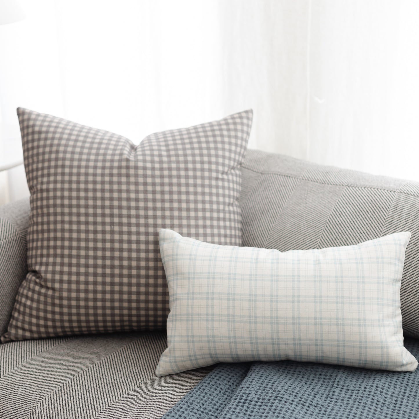 Gray and white gingham lumbar pillow displayed on gray textured sofa with coordinating pillows.