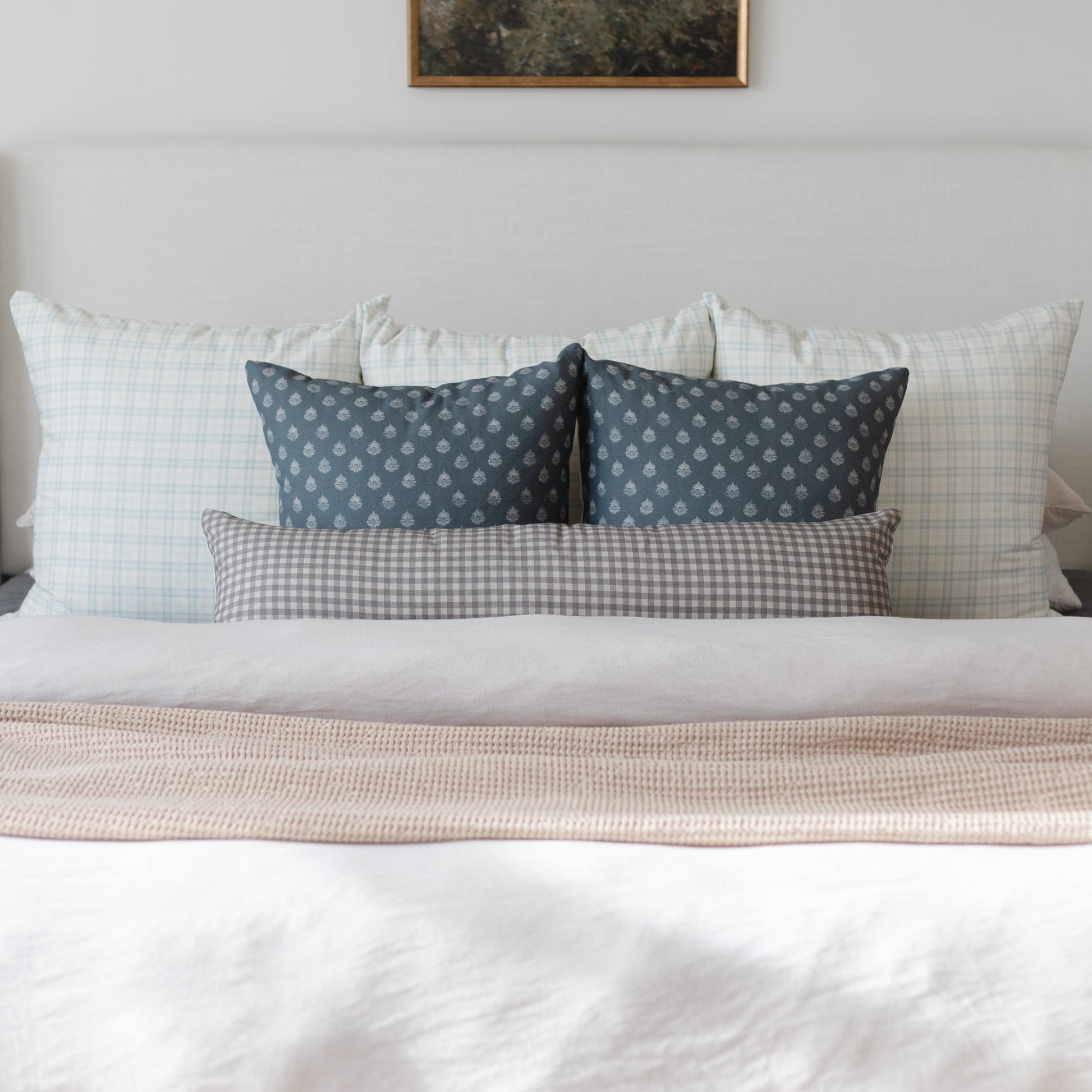 Blue patterned throw pillow displayed among coordinating pillows on a bed with neutral bedding.