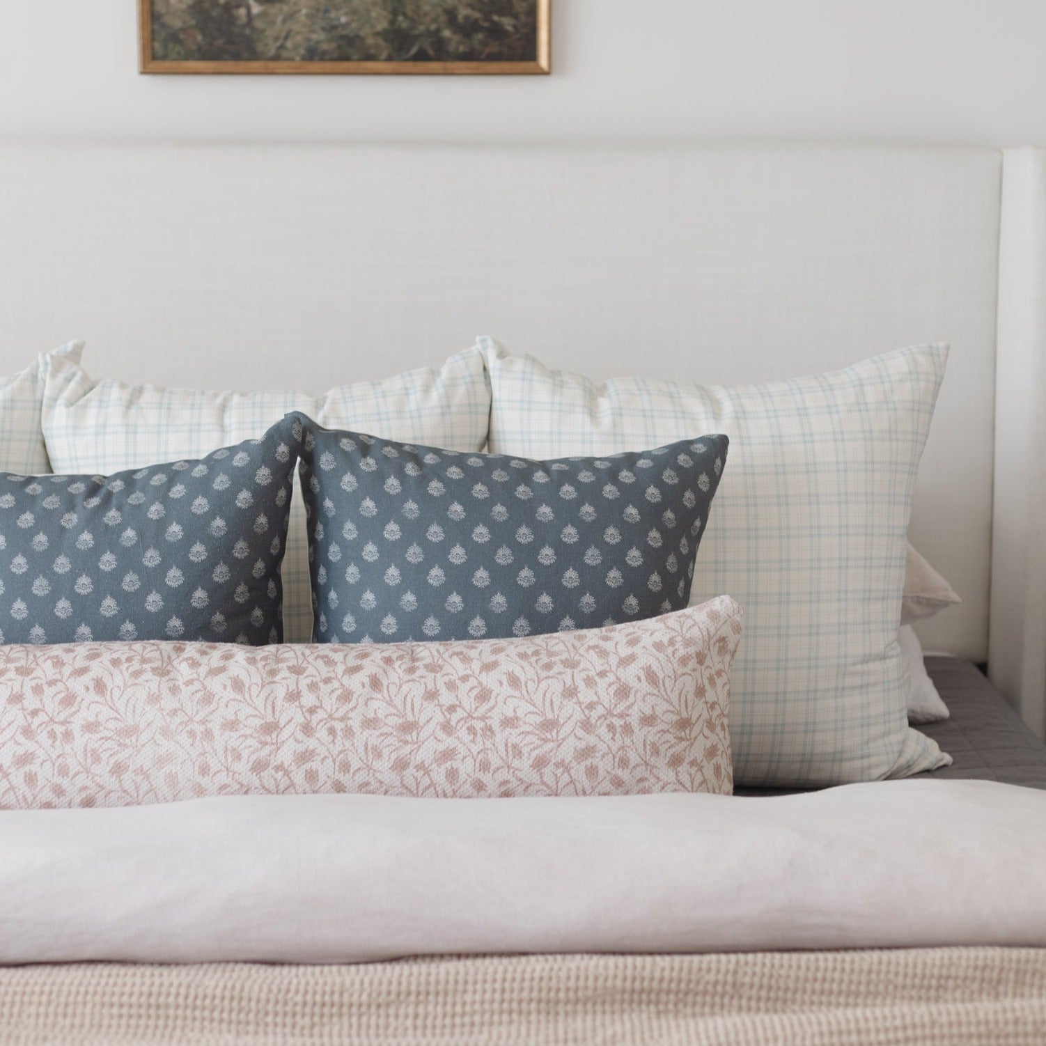 Decorative pillows with blue patterned, pink floral, and white checked designs arranged on a bed.