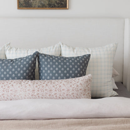 Decorative pillows with blue patterned, pink floral, and white checked designs arranged on a bed.