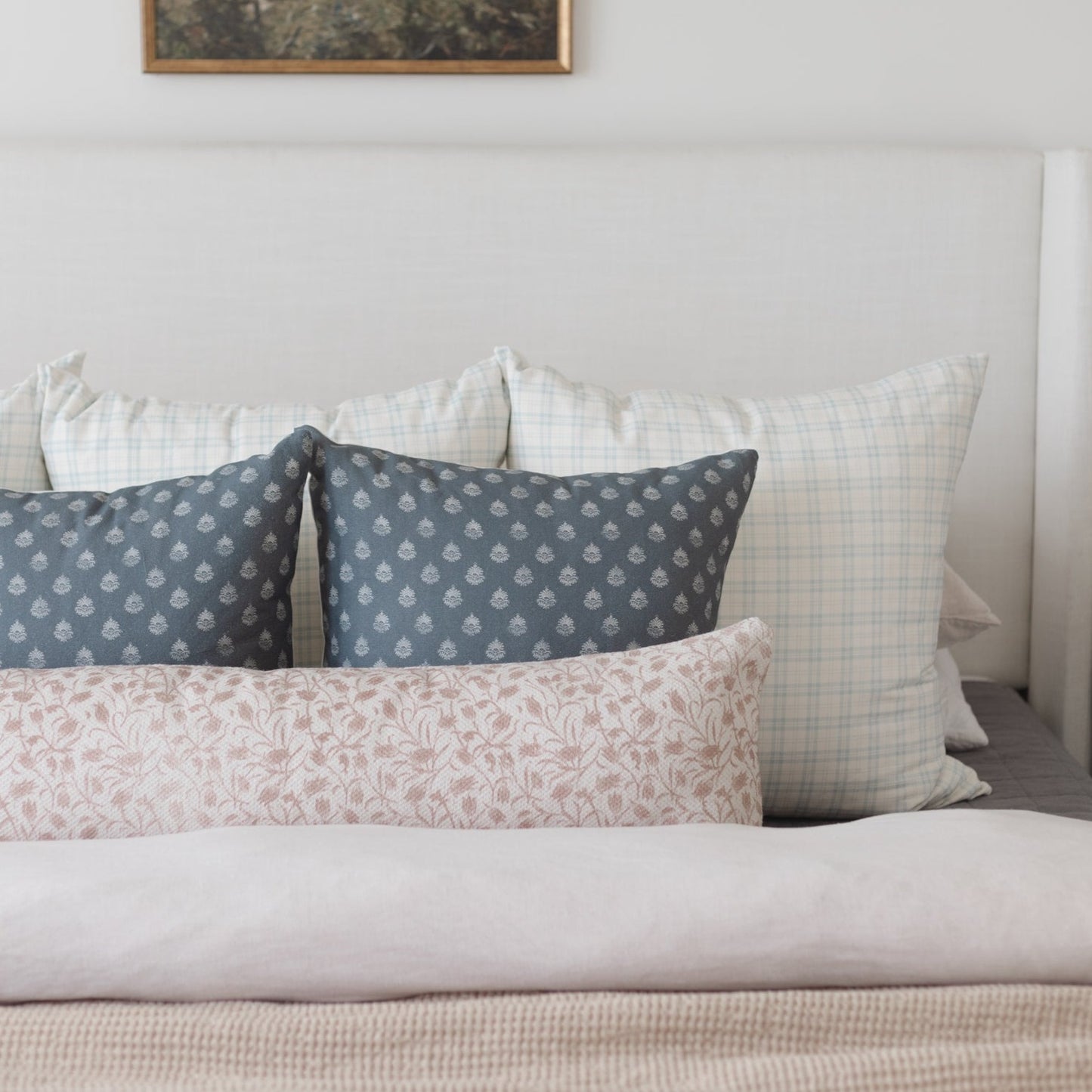 Bed with multiple decorative pillows in patterned fabrics: navy with damask print, light plaid, and pink floral designs.