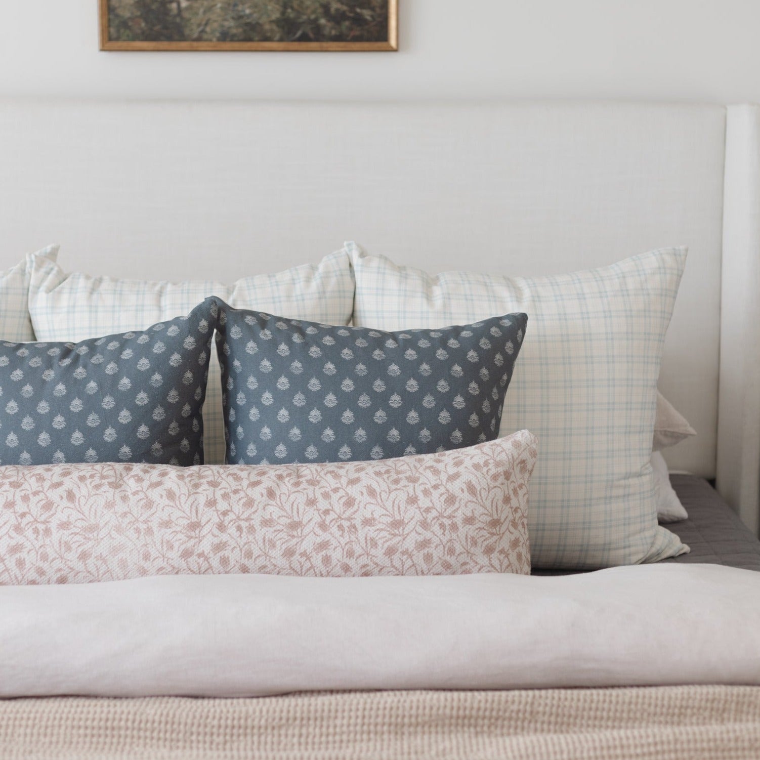 Bed with multiple decorative pillows in patterned fabrics: navy with damask print, light plaid, and pink floral designs.