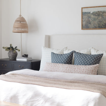 Beige textured throw blanket draped across foot of bed with white bedding and patterned pillows.