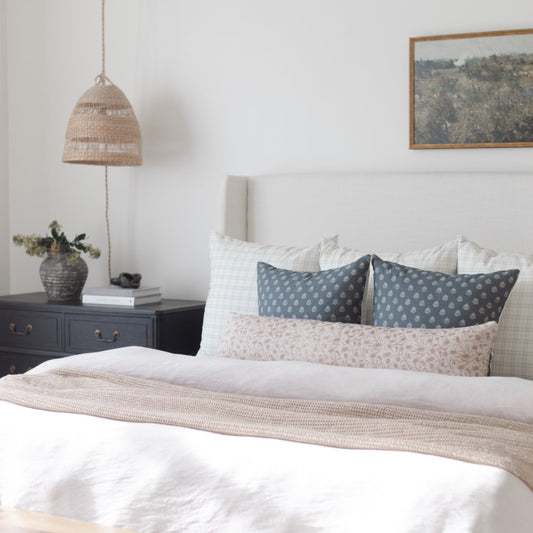 Beige textured throw blanket draped across foot of bed with white bedding and patterned pillows.