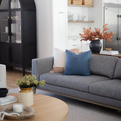 Navy blue square throw pillow on gray sofa in living room setting.