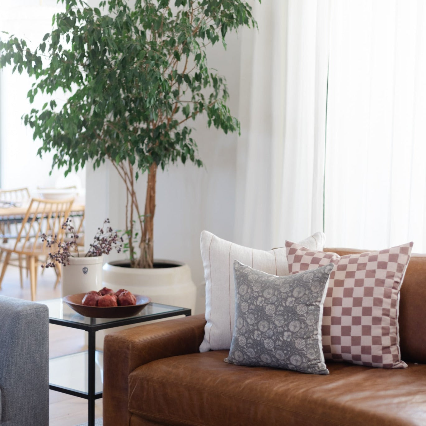 Tan and brown checkered throw pillow displayed on a cognac leather sofa next to a patterned gray pillow.