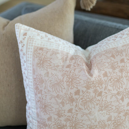 Cream and tan floral patterned pillow with decorative border on neutral-toned sofa.