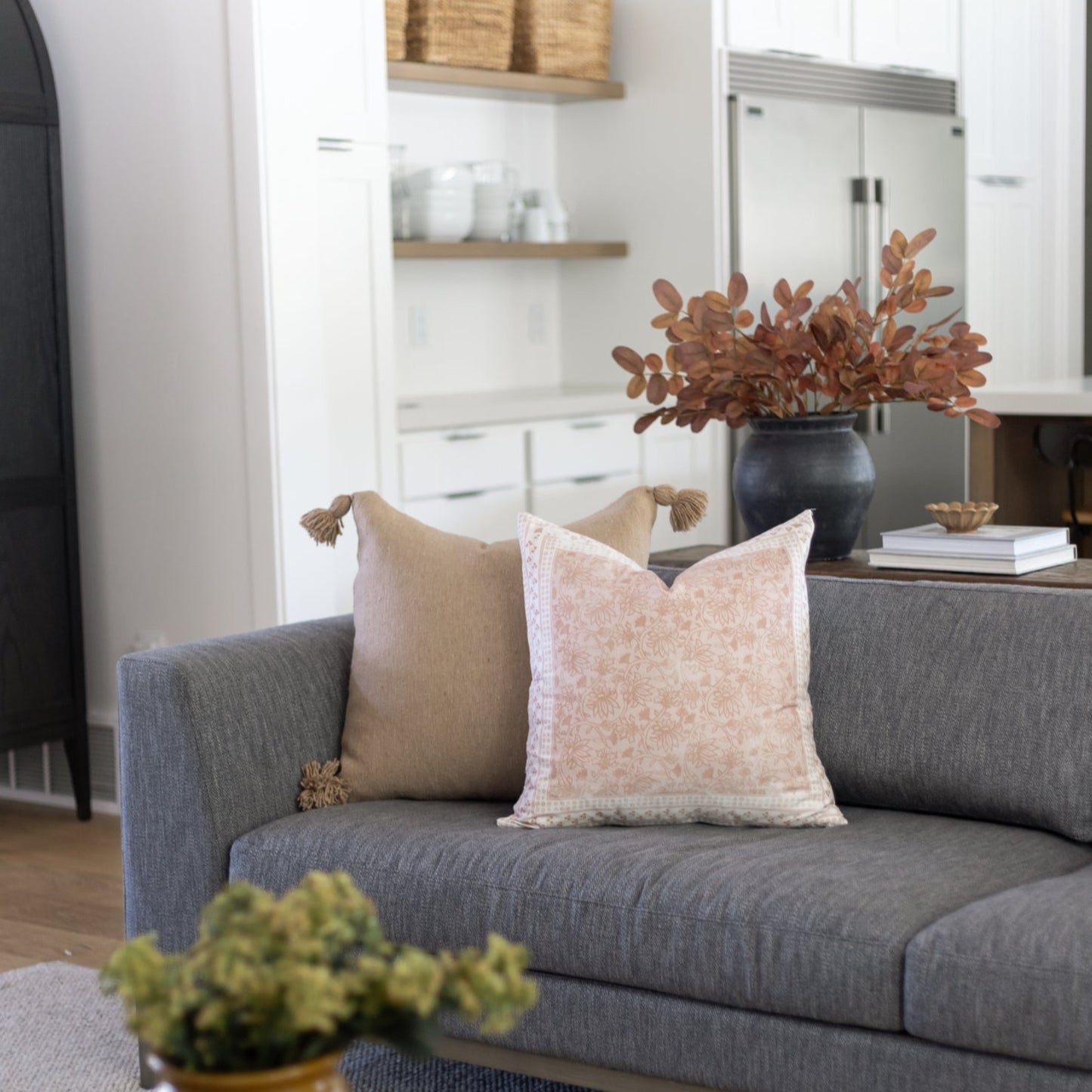 Beige and cream decorative pillows with tassel details arranged on a gray upholstered sofa.