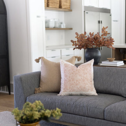Beige and cream decorative pillows with tassel details arranged on a gray upholstered sofa.