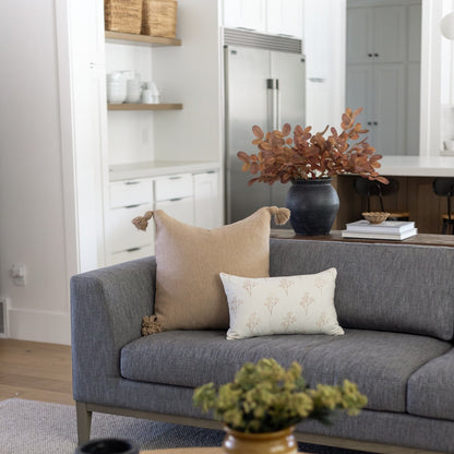 Cream lumbar pillow with tassel corners displayed on gray sofa with thistle pattern.