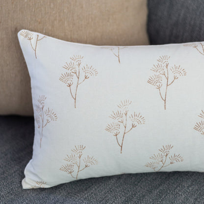 Cream lumbar pillow with tan thistle plant pattern, displayed on gray upholstered furniture.
