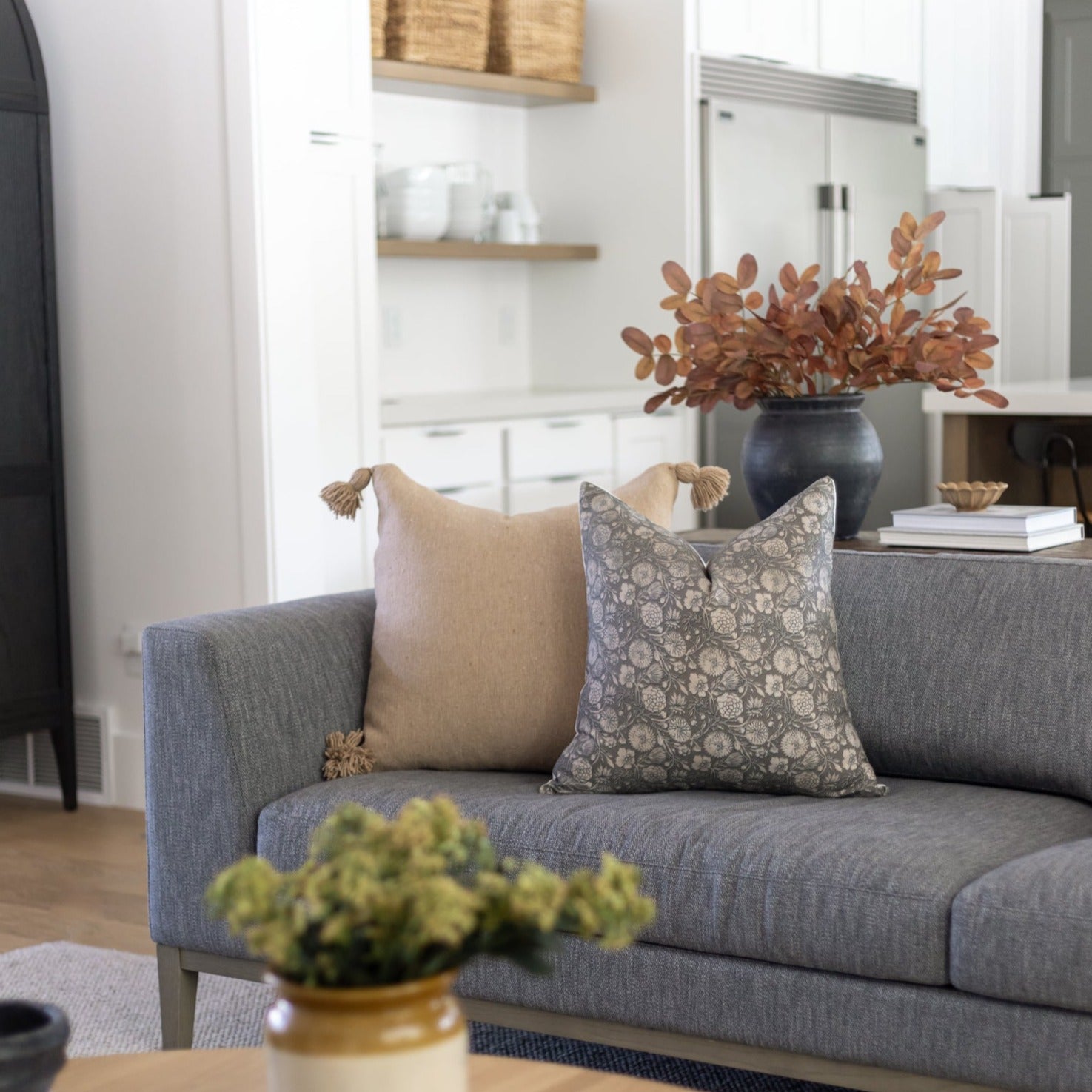 Two decorative pillows on a gray upholstered sofa, one beige with tassels and one gray patterned.