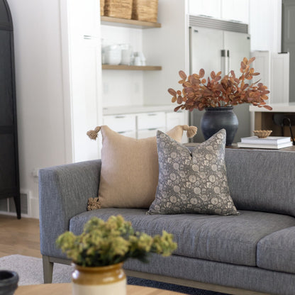 Two decorative pillows on a gray upholstered sofa, one beige with tassels and one gray patterned.