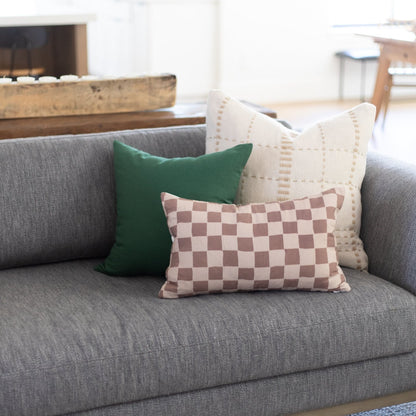 Three throw pillows on a gray sofa: solid green, checkerboard pink and white, and cream with geometric pattern.