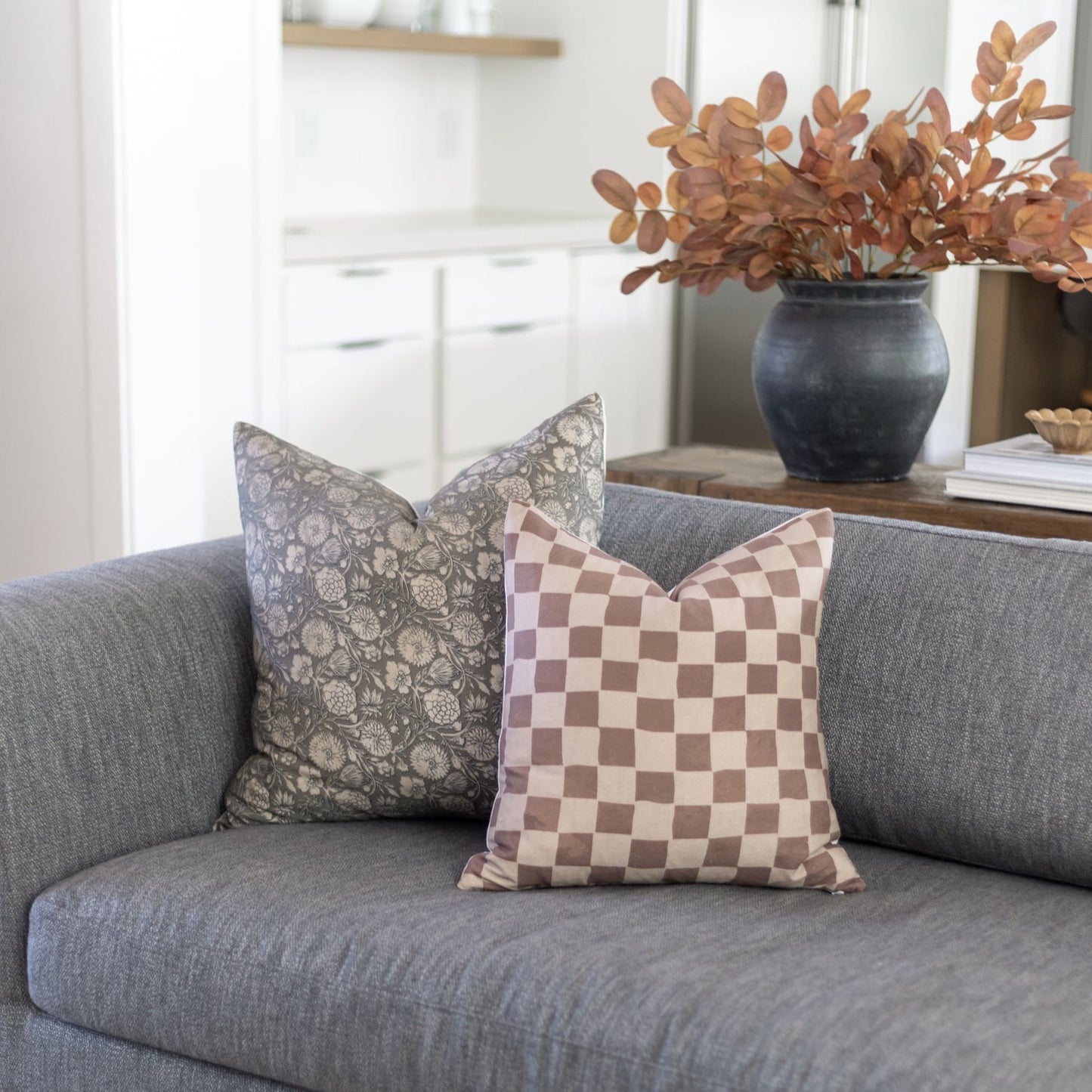 Tan and brown checkered pillow displayed on gray sofa next to patterned pillow.