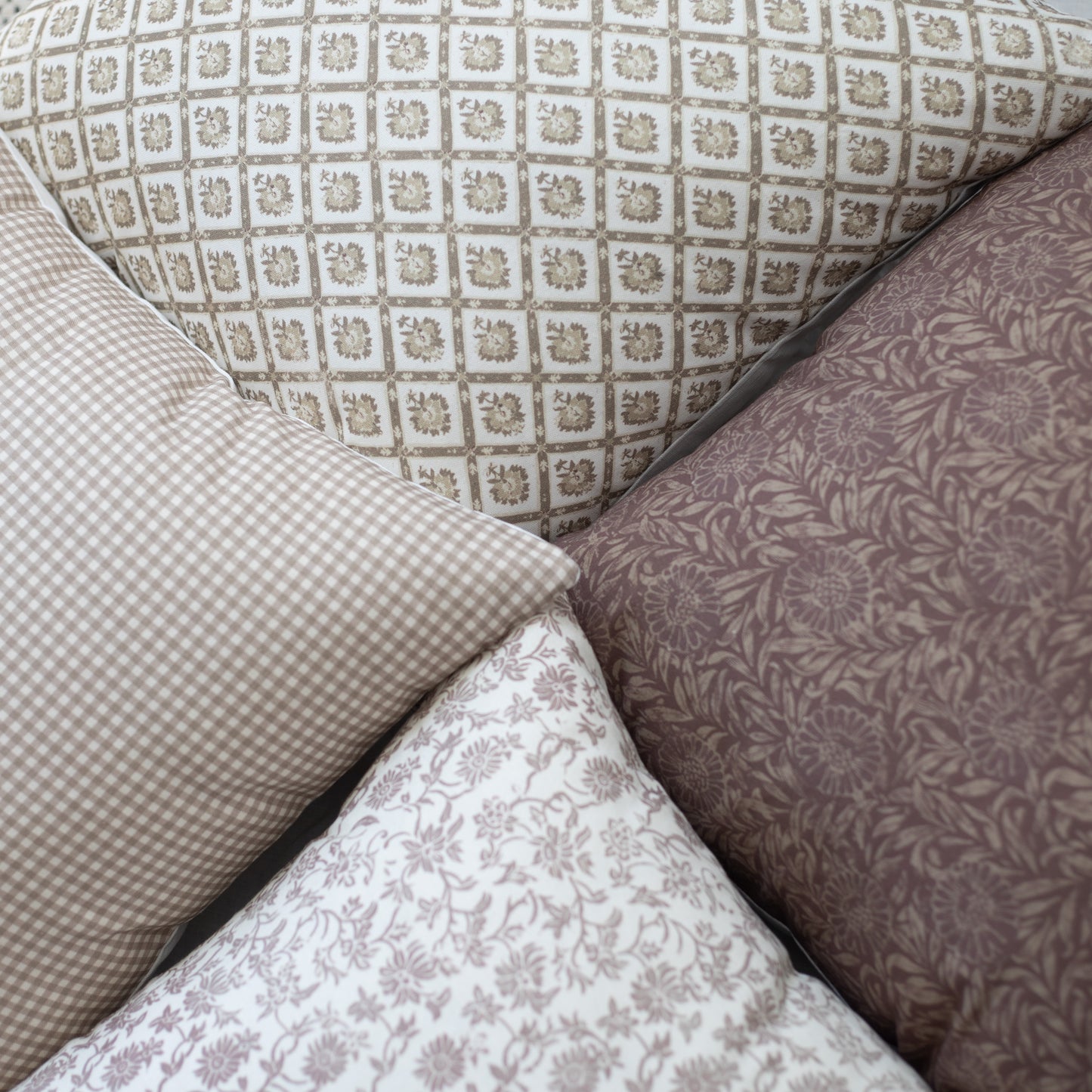Four decorative pillows with geometric and floral patterns in cream and taupe tones arranged together.