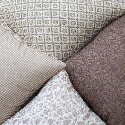 Four decorative pillows with geometric and floral patterns in cream and taupe tones arranged together.