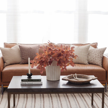 Four decorative pillows in neutral tones and patterns arranged on a tan leather sofa.