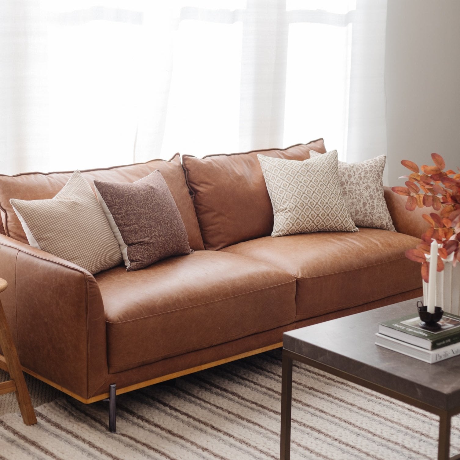 Four decorative pillows in varying patterns and textures arranged on a tan leather sofa.