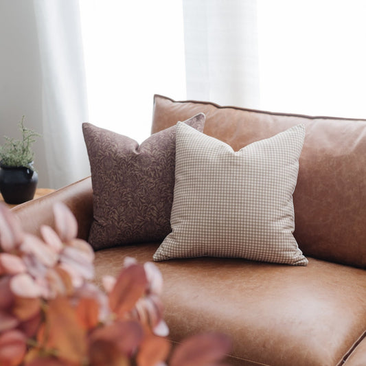 Tan and white gingham check pillow displayed on a brown leather sofa with coordinating pillows.