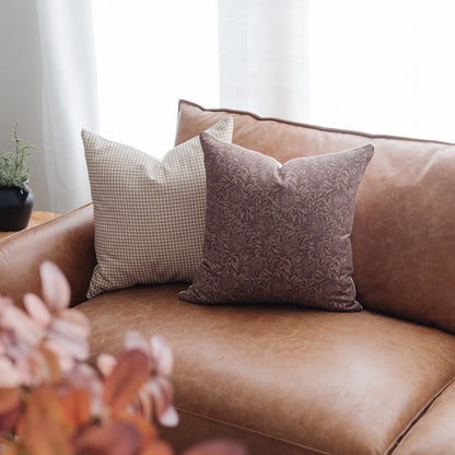 Two decorative pillows with gingham and floral patterns displayed on a tan leather sofa.