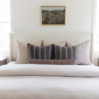 Tan and white gingham patterned pillow displayed on a bed with striped and textured pillows.