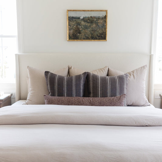 Tan and white gingham patterned pillow displayed on a bed with striped and textured pillows.