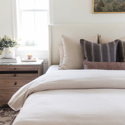 Tan and white gingham patterned pillow displayed on a bed with striped and solid throw pillows.