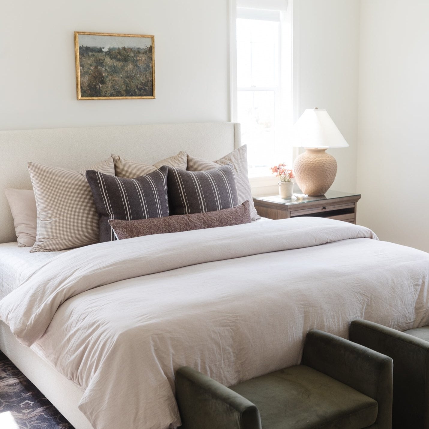 Tan and white gingham throw pillow arranged on a bed with striped and textured pillows.