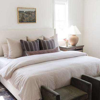 Tan and white gingham throw pillow arranged on a bed with striped and textured pillows.