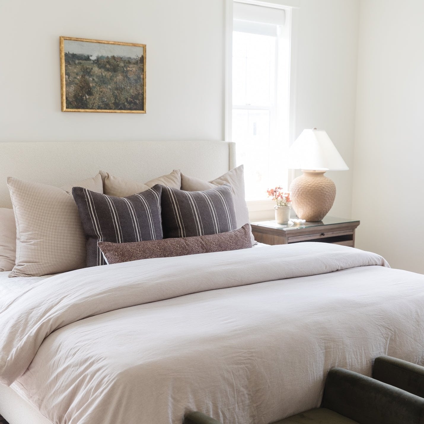 Striped lumbar pillow in charcoal and cream displayed on a bed with neutral bedding and coordinating pillows.