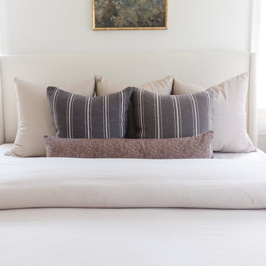 Tan and white gingham check pillow displayed on bed with striped and patterned accent pillows.