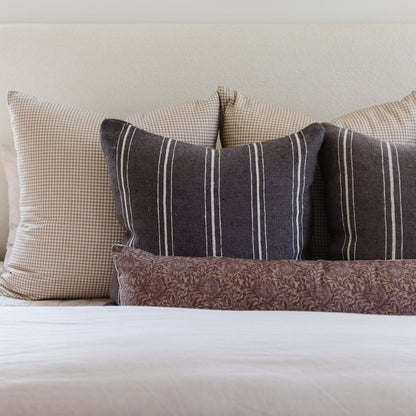 Tan and white gingham pillow displayed with striped and patterned pillows on a bed.