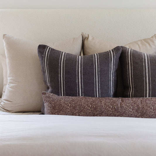 Tan and white gingham pillow displayed with striped and patterned pillows on a bed.