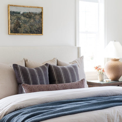 Rectangular lumbar pillow with navy blue and white vertical stripes, displayed on a bed with coordinating cushions.