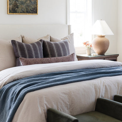Storm blue waffle-textured blanket draped across a bed with white linens and patterned pillows.