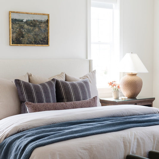 Tan and white gingham patterned decorative pillows arranged on a bed with striped bedding.