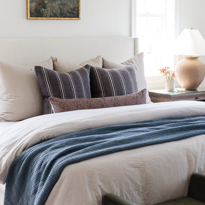 Charcoal striped lumbar pillow with white piping displayed on a bed with patterned bedding and neutral pillows.