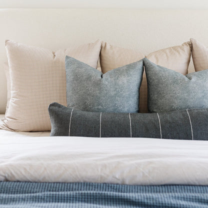 Gray and charcoal lumbar pillow with white vertical stripes arranged on a bed with checkered and solid pillows.