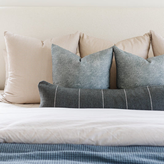 Gray and charcoal lumbar pillow with white vertical stripes arranged on a bed with checkered and solid pillows.
